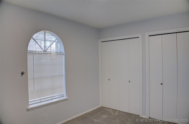 unfurnished bedroom featuring two closets, baseboards, and carpet floors