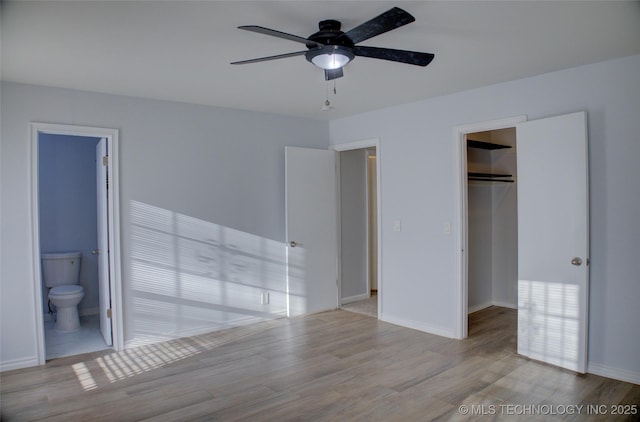 unfurnished bedroom featuring wood finished floors, baseboards, a spacious closet, a closet, and ensuite bathroom