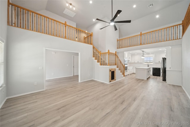 unfurnished living room featuring light wood finished floors, visible vents, ceiling fan, stairway, and high vaulted ceiling