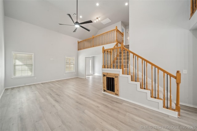 unfurnished living room with high vaulted ceiling, wood finished floors, baseboards, ceiling fan, and stairs