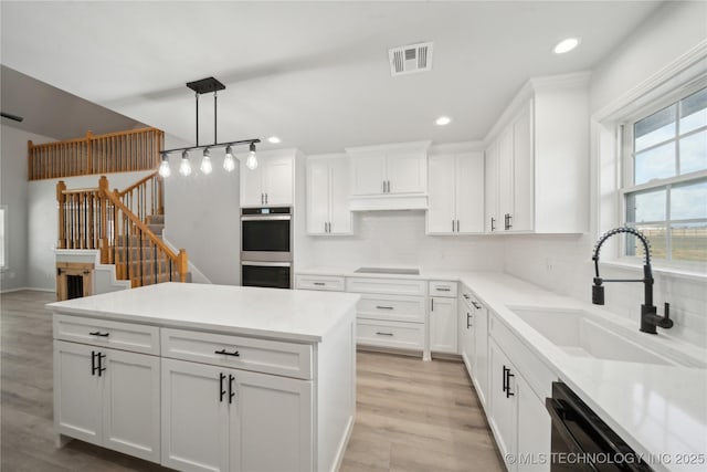 kitchen with visible vents, black appliances, a sink, white cabinets, and decorative backsplash