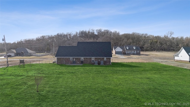 exterior space with brick siding, a lawn, a wooded view, and fence