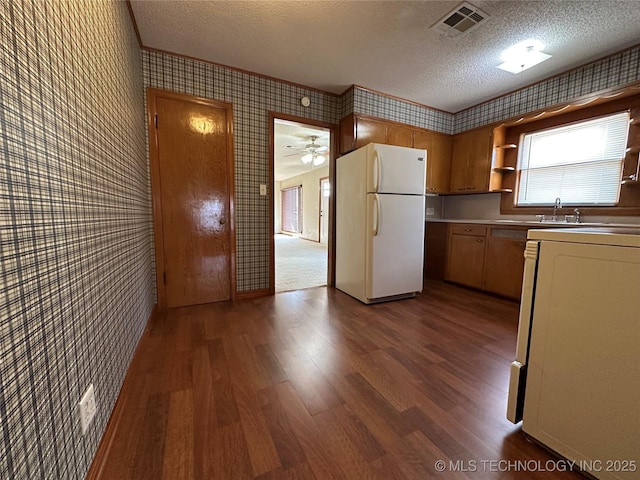 kitchen with wallpapered walls, visible vents, freestanding refrigerator, and a textured ceiling