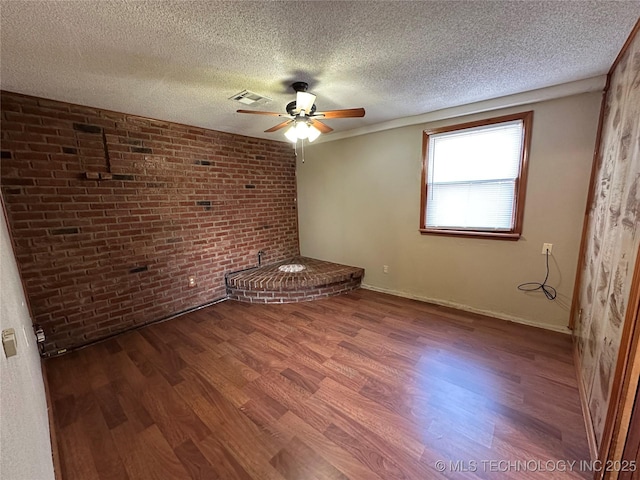 unfurnished bedroom featuring a ceiling fan, wood finished floors, visible vents, brick wall, and a textured ceiling