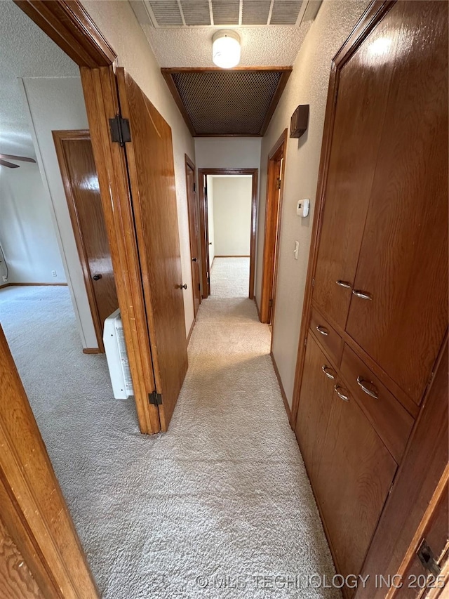 corridor with visible vents, light colored carpet, a textured ceiling, and baseboards