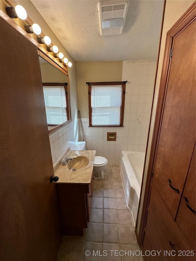 full bathroom with visible vents, tile patterned flooring, a textured ceiling, tile walls, and toilet