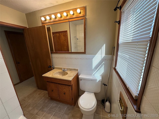 bathroom featuring tile patterned floors, toilet, a textured ceiling, tile walls, and vanity