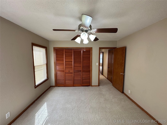 unfurnished bedroom featuring a closet, baseboards, a textured ceiling, and light carpet