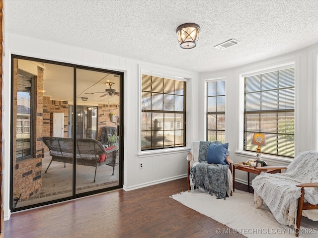 living area with wood finished floors, visible vents, a wealth of natural light, and a textured ceiling