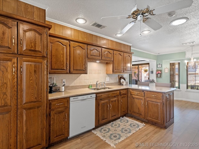 kitchen featuring brown cabinetry, visible vents, white dishwasher, and a sink