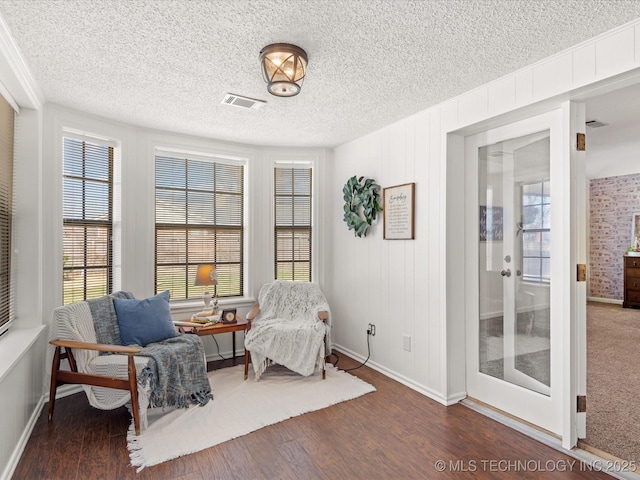 sitting room featuring visible vents, a textured ceiling, baseboards, and wood finished floors