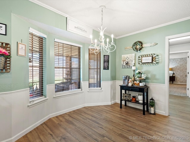 dining area featuring a notable chandelier, ornamental molding, wood finished floors, and a wainscoted wall