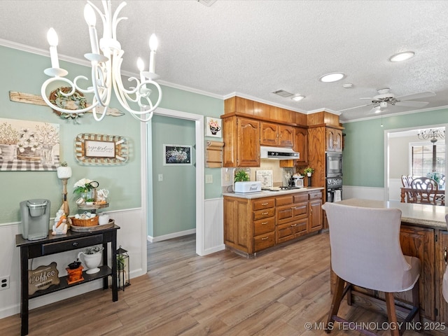 kitchen featuring light wood finished floors, brown cabinetry, a wainscoted wall, and under cabinet range hood