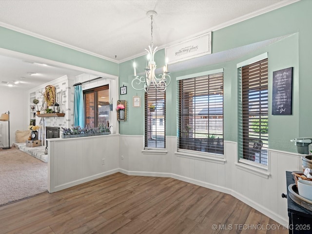 unfurnished dining area with an inviting chandelier, ornamental molding, wainscoting, and wood finished floors
