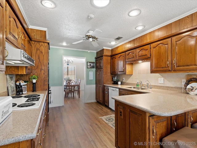 kitchen featuring crown molding, wainscoting, brown cabinets, white appliances, and a sink