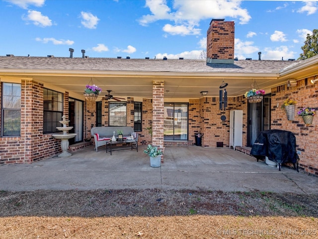 rear view of house featuring ceiling fan, a patio, brick siding, and a chimney