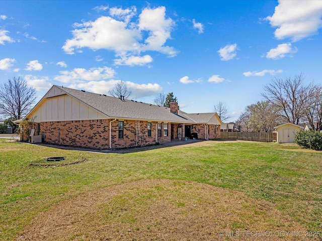 rear view of house with fence, a yard, a chimney, an outdoor structure, and brick siding