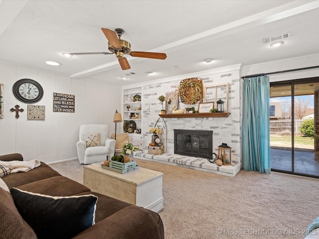 living area with visible vents, carpet, built in features, a glass covered fireplace, and a ceiling fan