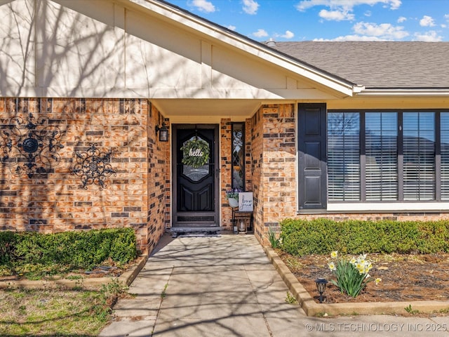 doorway to property featuring brick siding and a shingled roof