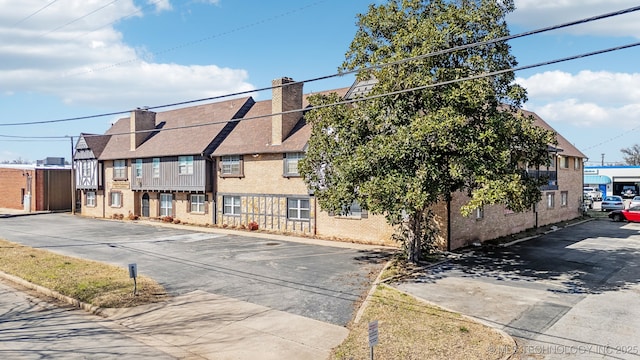 townhome / multi-family property featuring roof with shingles, uncovered parking, a residential view, a chimney, and brick siding