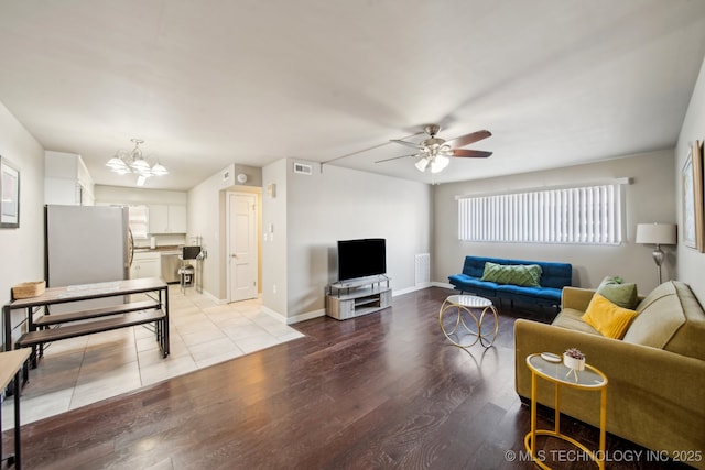 living area with visible vents, light wood-style flooring, ceiling fan with notable chandelier, and baseboards