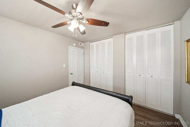 bedroom with two closets, dark wood-style floors, and a ceiling fan