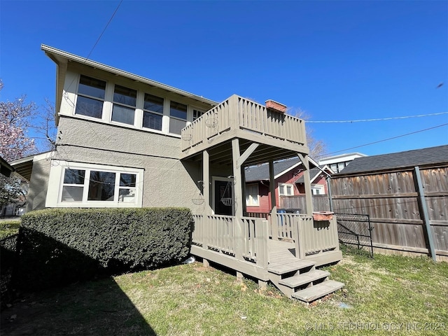 back of house with stucco siding, a yard, a wooden deck, and fence