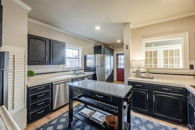 kitchen featuring tile counters, appliances with stainless steel finishes, dark cabinetry, and a sink