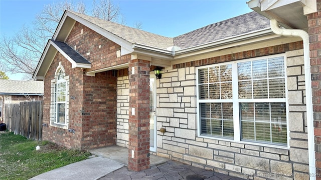 view of home's exterior featuring fence, brick siding, stone siding, and a shingled roof