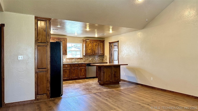 kitchen featuring a center island, a textured wall, appliances with stainless steel finishes, wood finished floors, and a sink