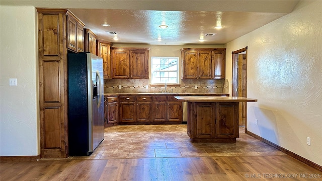 kitchen featuring tasteful backsplash, stainless steel fridge with ice dispenser, a textured wall, wood finished floors, and a sink