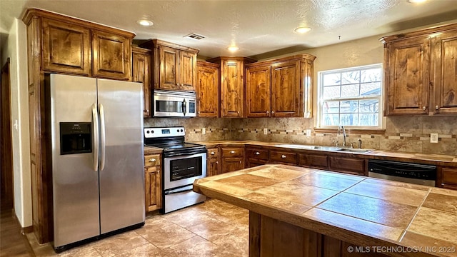 kitchen featuring brown cabinetry, visible vents, a sink, decorative backsplash, and appliances with stainless steel finishes