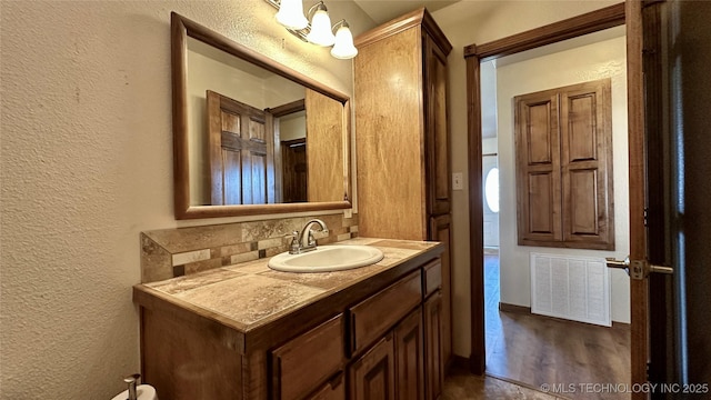 bathroom with visible vents, a textured wall, decorative backsplash, wood finished floors, and vanity