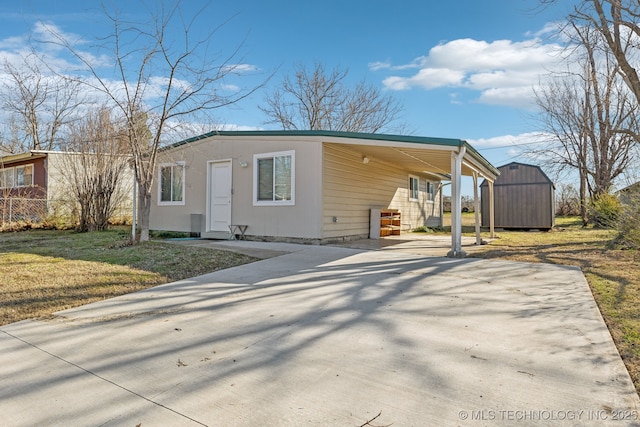 view of front of property with a front lawn, a shed, concrete driveway, a carport, and an outbuilding