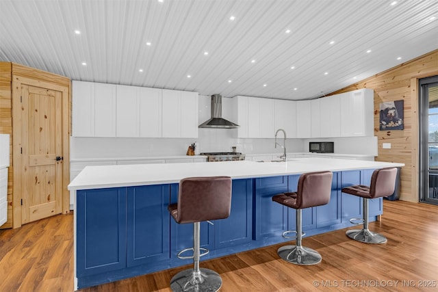 kitchen with light wood-style flooring, wood walls, light countertops, and wall chimney exhaust hood