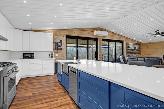 kitchen featuring blue cabinets, a wall mounted AC, stainless steel appliances, wood walls, and vaulted ceiling