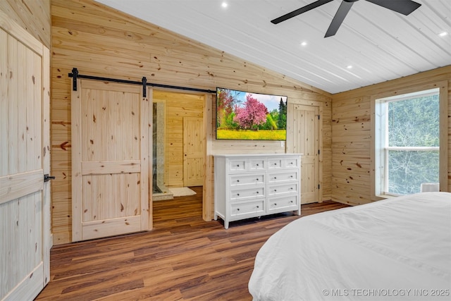 bedroom with wooden walls, a barn door, vaulted ceiling, recessed lighting, and wood finished floors