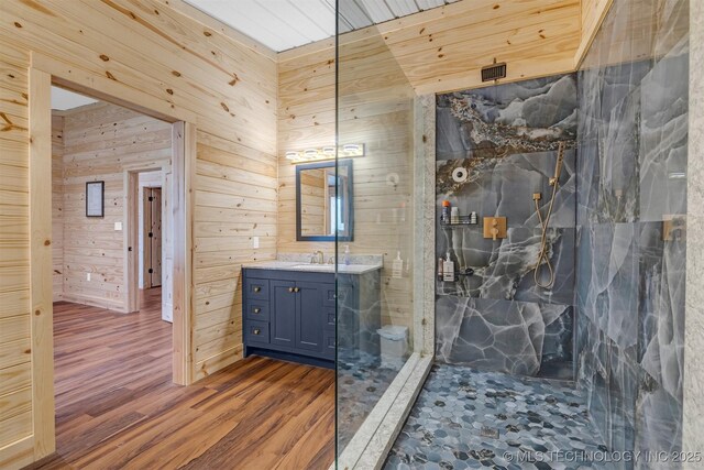 bathroom with vanity, wood finished floors, visible vents, a marble finish shower, and wood walls