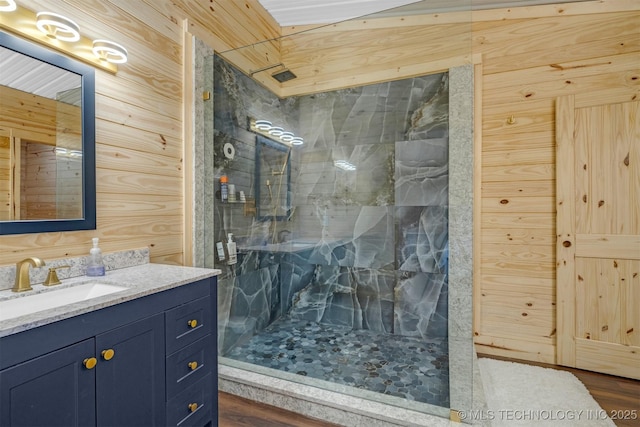 bathroom with a marble finish shower, wood walls, and vanity