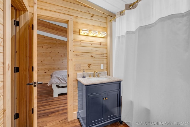 ensuite bathroom with vanity, wooden walls, wood finished floors, and curtained shower