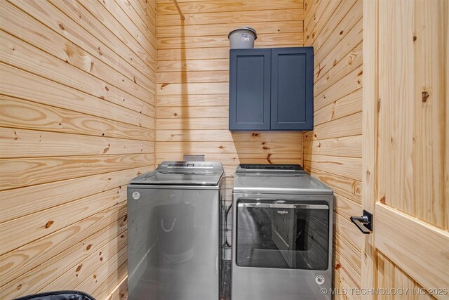 clothes washing area with wooden walls, cabinet space, and washer and clothes dryer