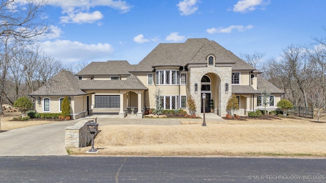 french country style house with stucco siding, stone siding, roof with shingles, and driveway