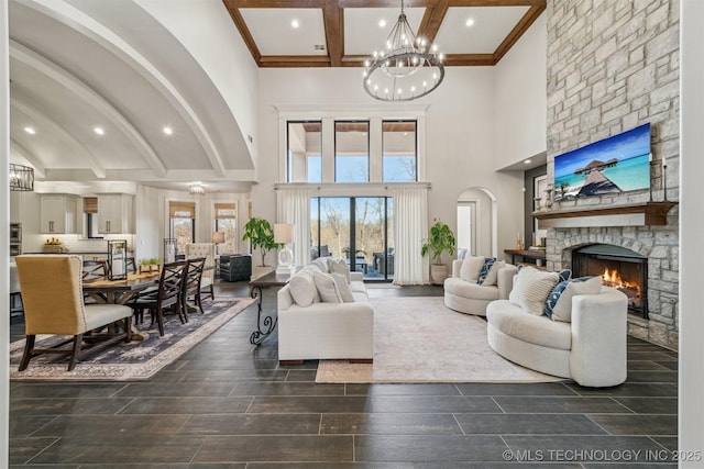 living area featuring wood finish floors, beamed ceiling, a stone fireplace, a towering ceiling, and a notable chandelier