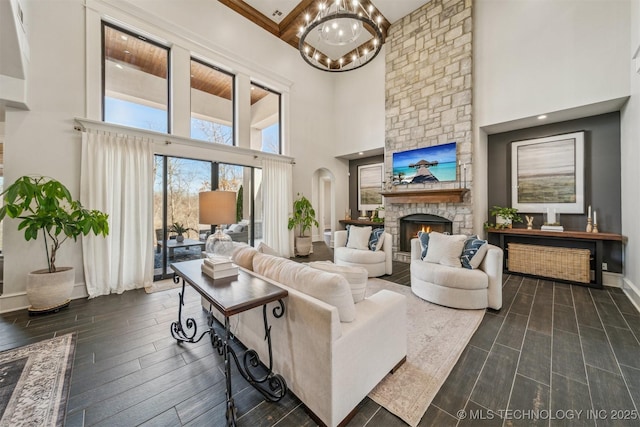 living room with wood finish floors, arched walkways, a stone fireplace, an inviting chandelier, and baseboards