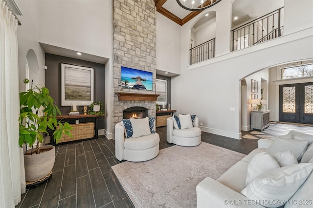 living area featuring french doors, baseboards, a stone fireplace, and wood tiled floor