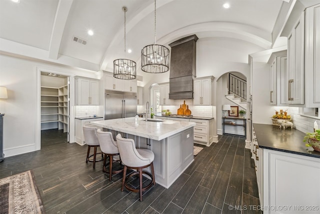 kitchen with baseboards, visible vents, custom exhaust hood, a kitchen island with sink, and stainless steel appliances