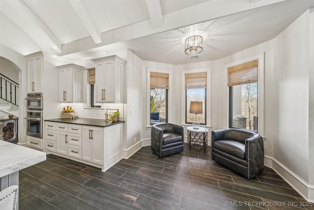 kitchen featuring stainless steel double oven, backsplash, baseboards, and beamed ceiling