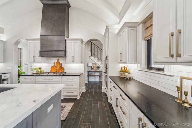 kitchen featuring custom exhaust hood, wood finish floors, dark stone counters, and stainless steel gas cooktop