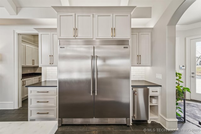 kitchen with dark wood-type flooring, stainless steel built in refrigerator, dark countertops, decorative backsplash, and baseboards