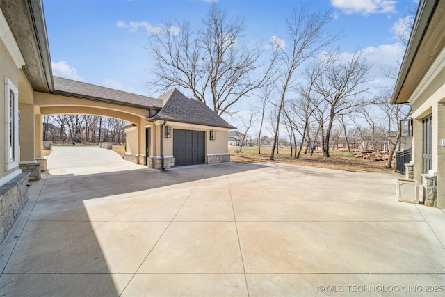 view of patio with concrete driveway, an outbuilding, and a garage